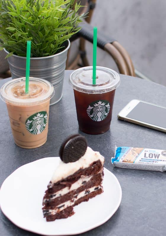 Side view of two iced coffee drinks and a slice of cake on a table.