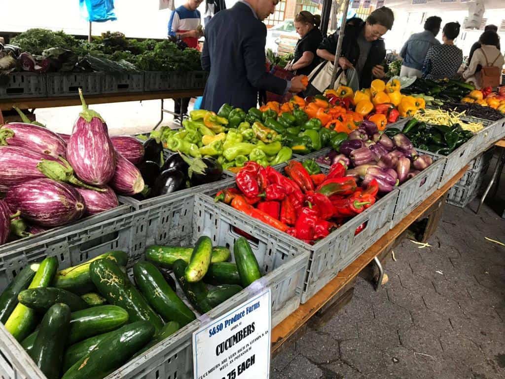 picture of Cheap food at the farmers market. Eggplants, cucumber, red bell peppers, and green peppers.
