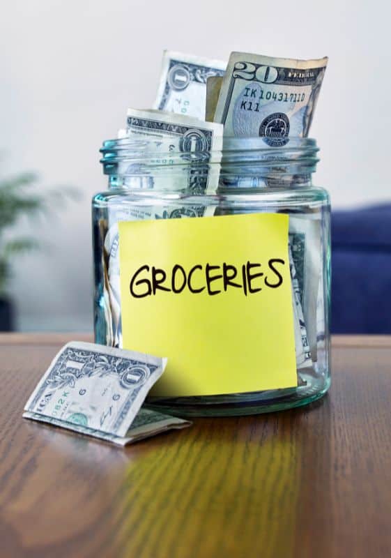 Money saved for groceries in a glass jar.