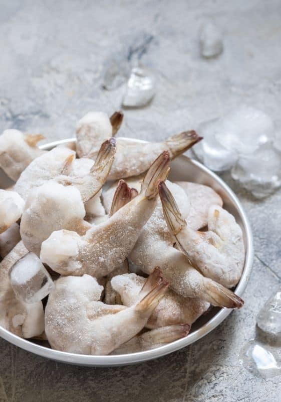 Frozen uncooked shrimps on a white bowl.