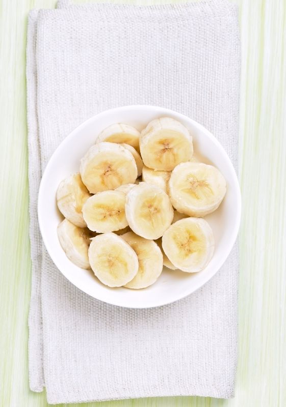 Top view of sliced bananas in a white bowl.