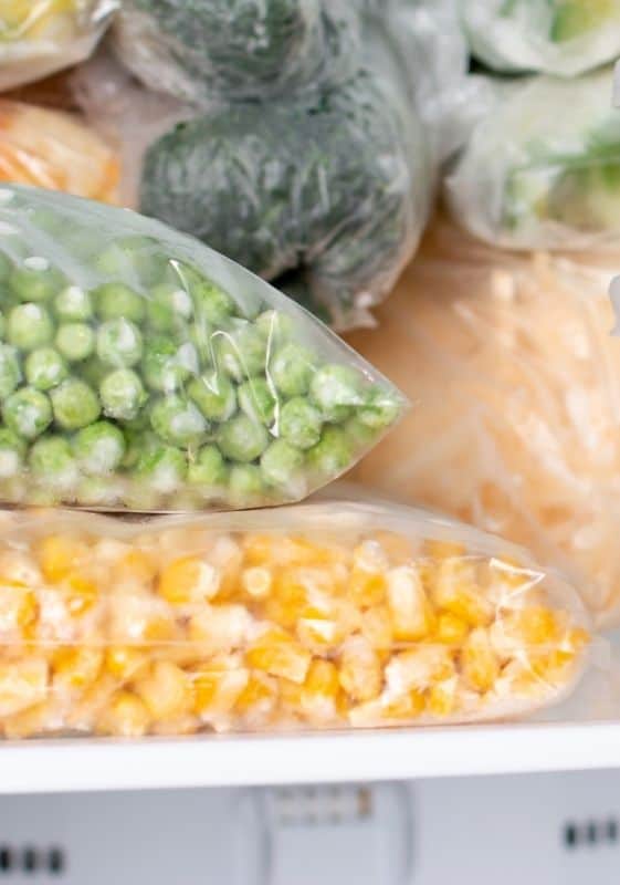 Bags of frozen corn and frozen peas in the freezer.