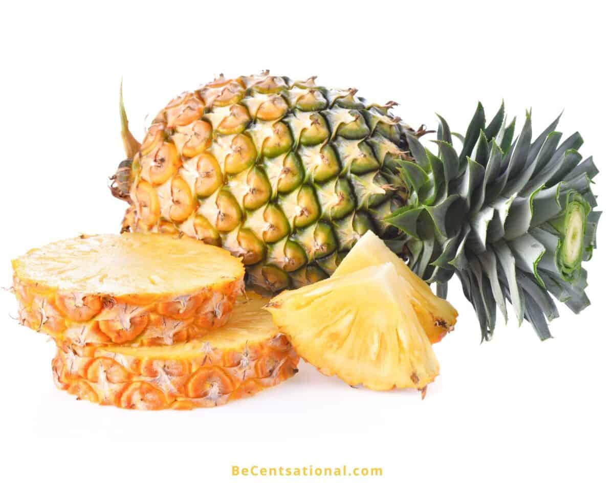 One whole pineapple and a few pineapple slices on a white background. Yellow foods.
