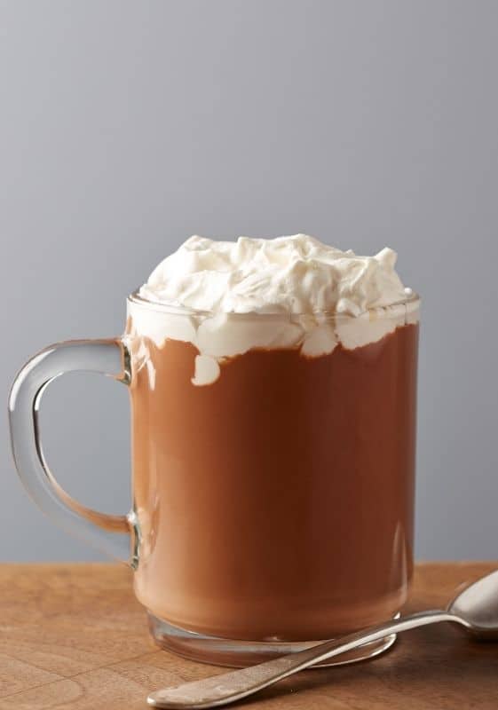 Cup of hot cocoa topped with frozen whipped cream.