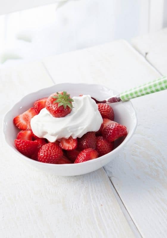 Strawberries topped with whipped cream in a white bowl on a white background. What to do with whipped cream.