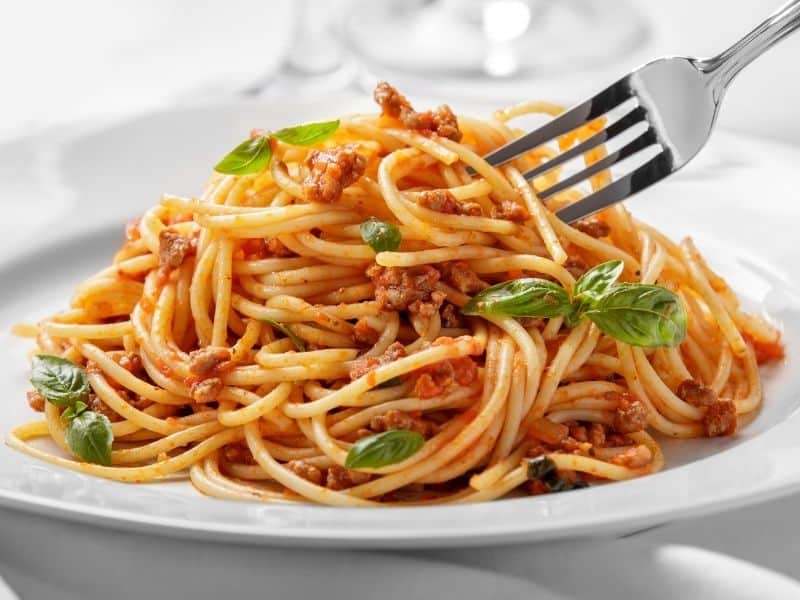 Spaghetti in marinara sauce garnished with basil served in a white plate. Can You Cook Pasta in the Sauce?