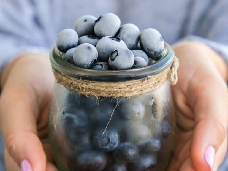 Side view image of woman holding a glass jar of frozen blueberries.