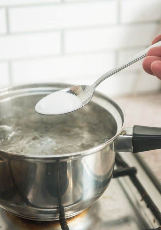 Adding salt to boiling water to cook pasta.