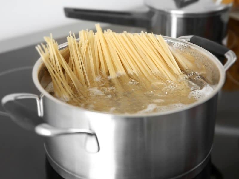 Pot of hot water boiling with spaghetti on stove top.