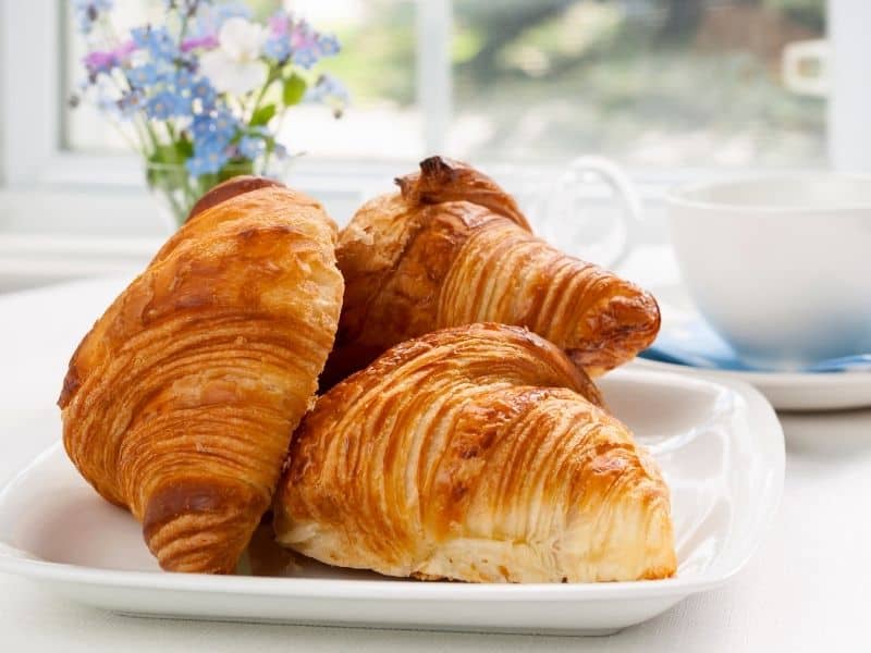 Three baked croissants on a white plate. Can You Freeze Croissants?