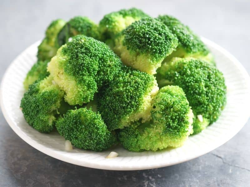 Steamed broccoli florets on a white plate. how to steam broccoli without a steamer.