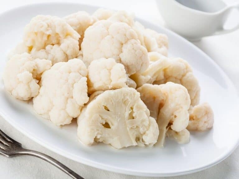 Steamed cauliflower on a white plate and white background. how to steam cauliflower without a steamer.