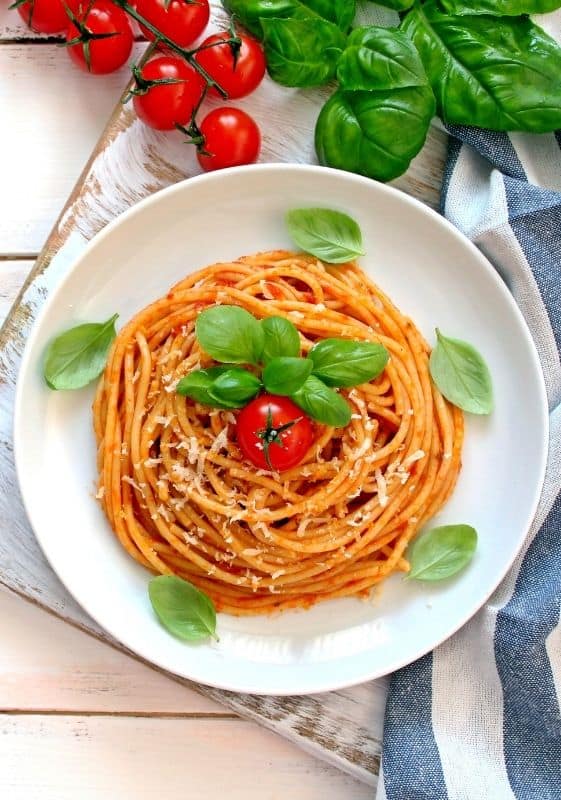 Top view of Spaghetti Pomodoro served on a white plate and garnished with fresh basil leaves and a cherry tomato on a white background with basil leaves and tomato vine.