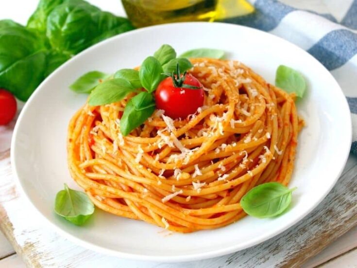 Aerial view of Spaghetti Pomodoro served on a white plate and garnished with fresh basil leaves and a cherry tomato.