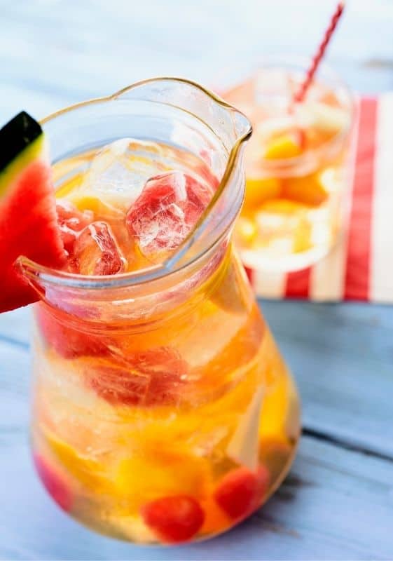 Pitcher of Sparkling Wine Sangria decorated with a slice of watermelon on a blue background.