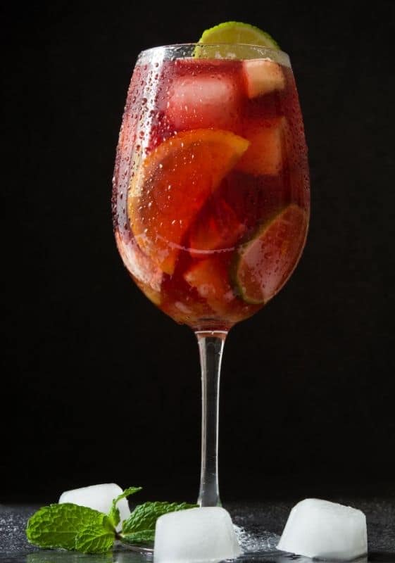 A wine glass of Spanish sangria with citrus fruits on a a dark background.