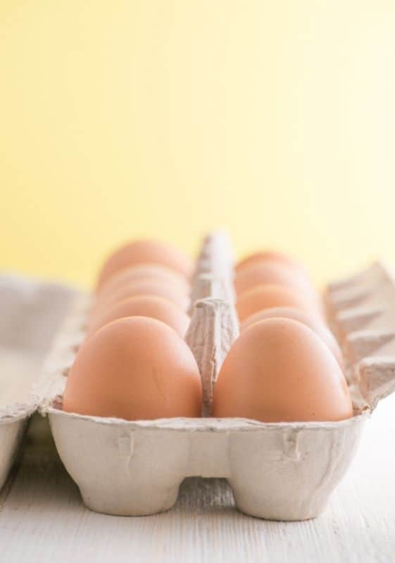 Brown eggs in carton on a yellow background.