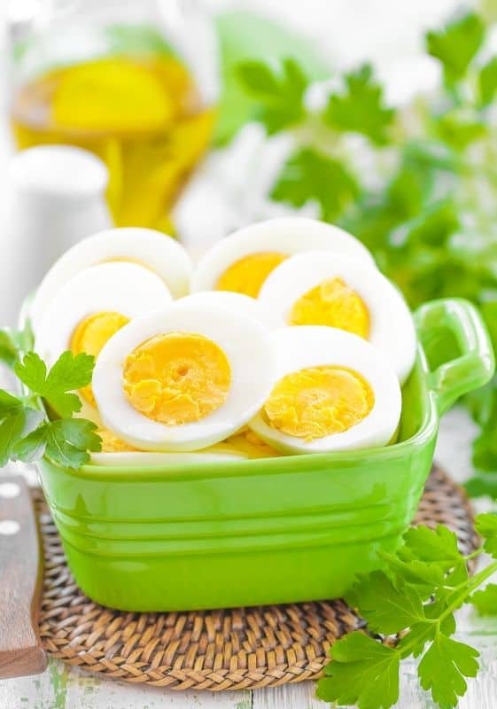 Boiled eggs cooked in the microwave cut in half served on a green container and garnished with parsley.