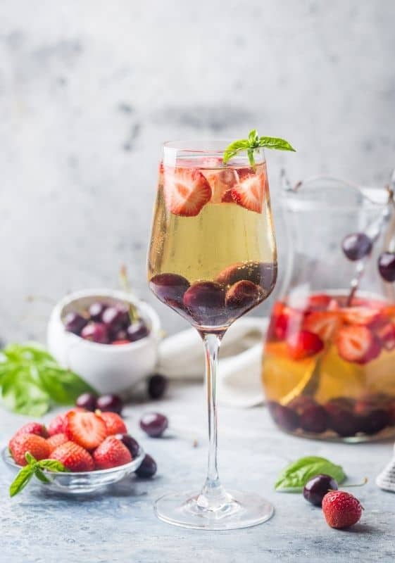 Sweet tea sangria pitcher and whine glass with strawberries and cherries on a gray background showcasing the berries.