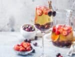 Sweet tea sangria pitcher and whine glass with strawberries and cherries on a gray background showcasing the berries.