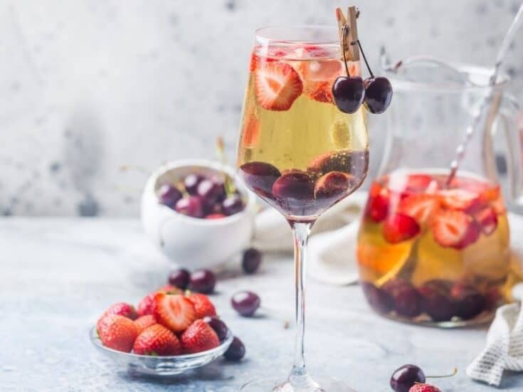 Sweet tea sangria pitcher and whine glass with strawberries and cherries on a gray background showcasing the berries.