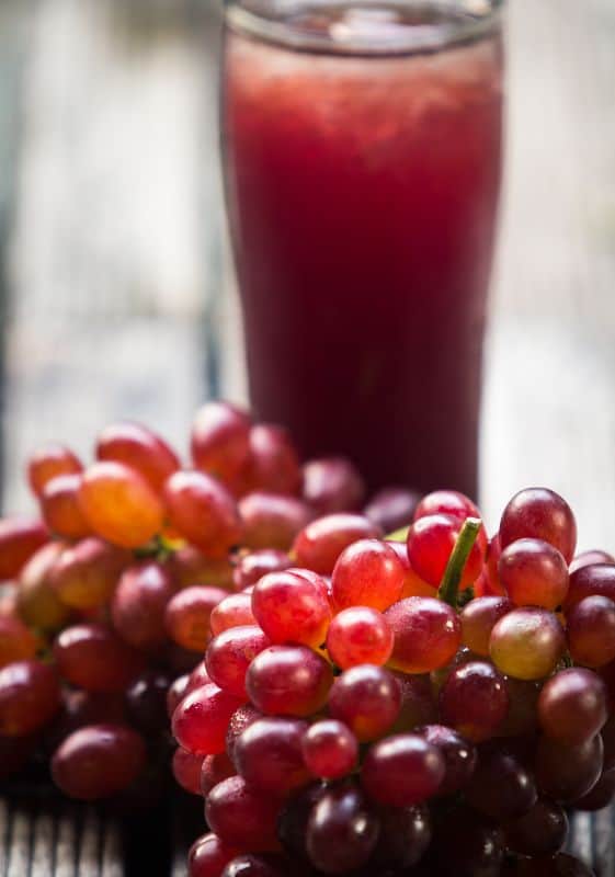 A tall glass of grape juice made from concentrate with grapes placed in front of the glass.