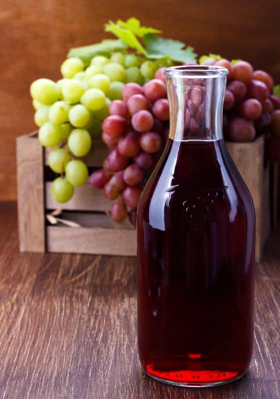 A carafe of grape juice made from concentrate with grapes on the background.