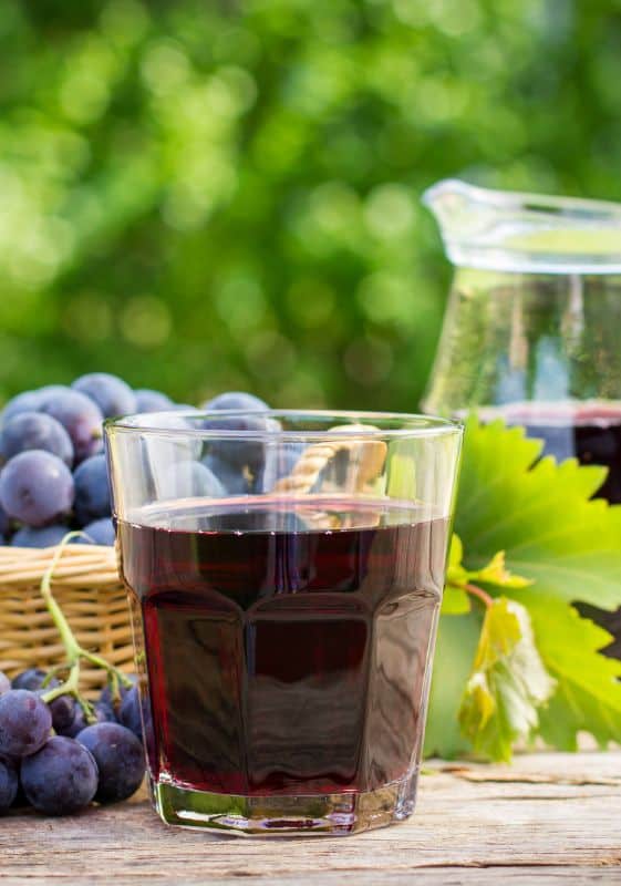 Side view of a pitcher and glass of grape juice with a basket full of grapes by the side all on a wooden table. Side view of a glass full of grape juice and grapes on the vine on the side. Does Grape Juice Concentrate Expire?
