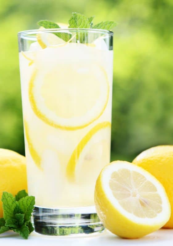 A tall glass of lemonade with half lemons as prop on the table.
