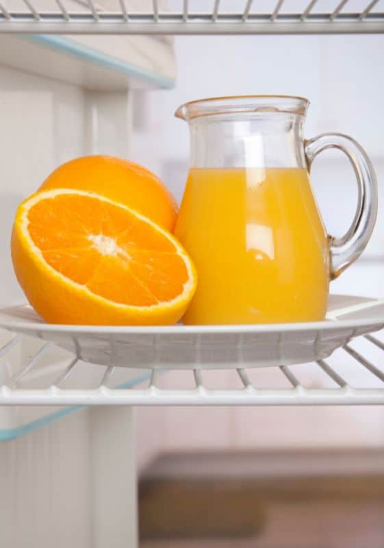 Pitcher of orange juice and oranges inside a refrigerator.