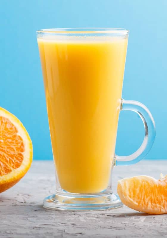 Tall glass of orange juice with a blue background.