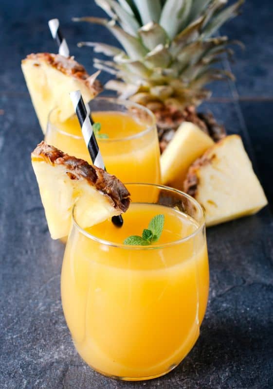 two small glasses of pineapple juice and a pineapple on the background.