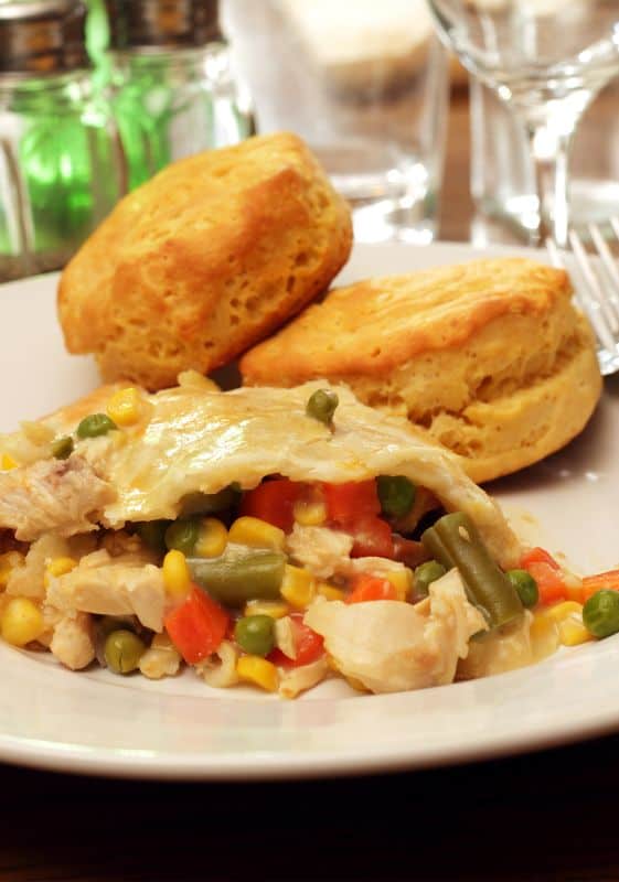 A single slice of crescent roll chicken pot pie in a white plate set on a wooded table with biscuits.