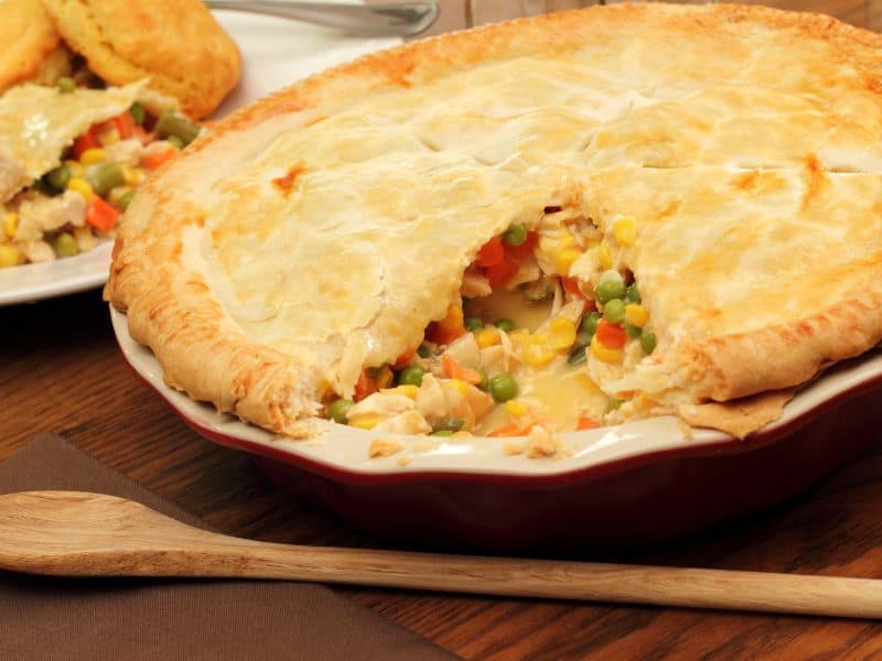 Side view of sliced crescent roll chicken pot pie in a round baking dish set on a wooded table.