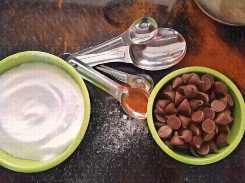 Measuring spoons in different sizes next to a bowl of chocolate chips and sugar. How many tsp are in a tbsp.