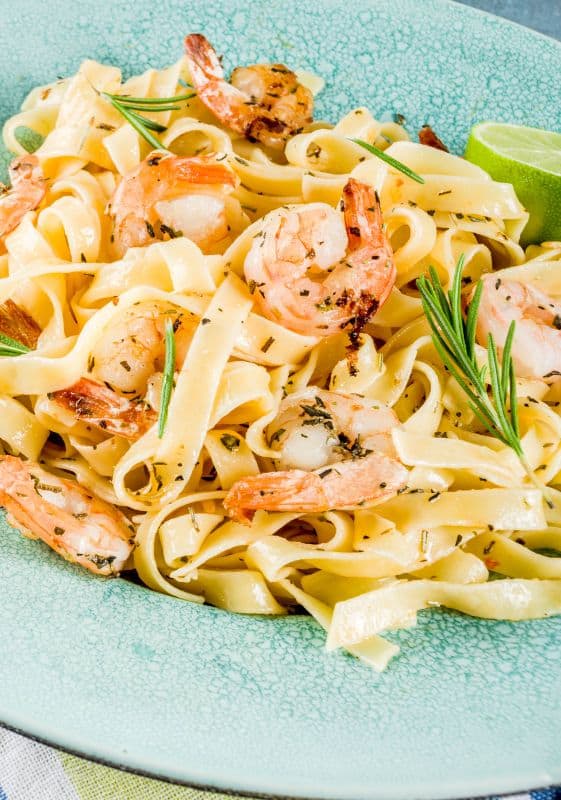 Close-up of large, perfectly cooked shrimp coated in a golden garlic and butter sauce, served on a bed of linguini.