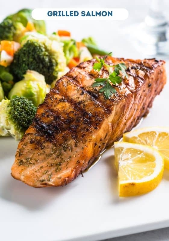 Grilled salmon with vegetables and lemon slices on a white plate. The perfect Saturday night dinner for two.