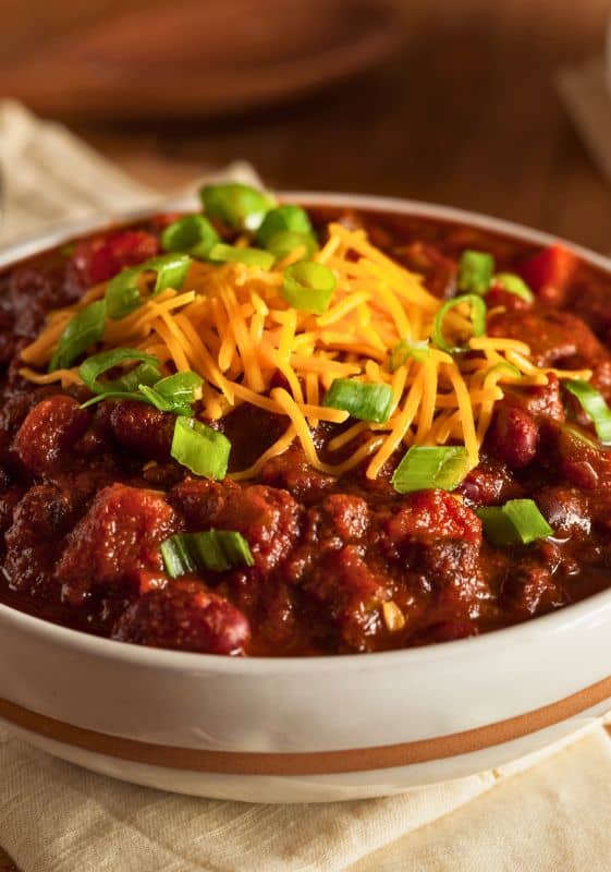 White bowl of beef chili topped with cheese.