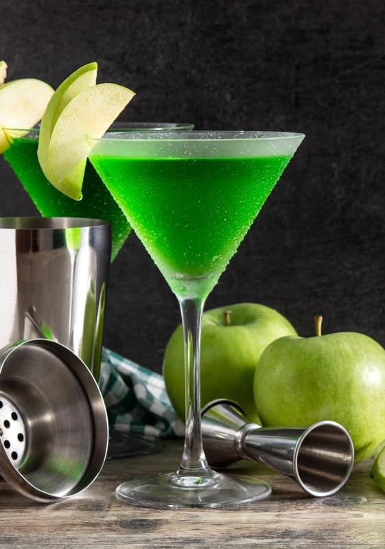 Garnished Appletini with Green Apple Slices
Description: A beautifully presented Appletini cocktail is showcased in a martini glass. The drink is adorned with thin slices of green apple, carefully arranged on the rim of the glass. 