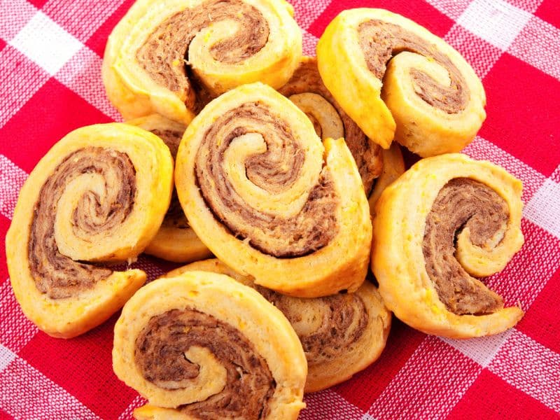 Image of a close-up of a sausage pinwheel. The pinwheel is cut in half and the layers of crescent roll, sausage, and cream cheese are visible.