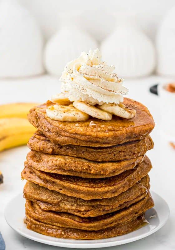 Sweet potato pancakes stacked up and topped with sliced bananas and whipped cream.