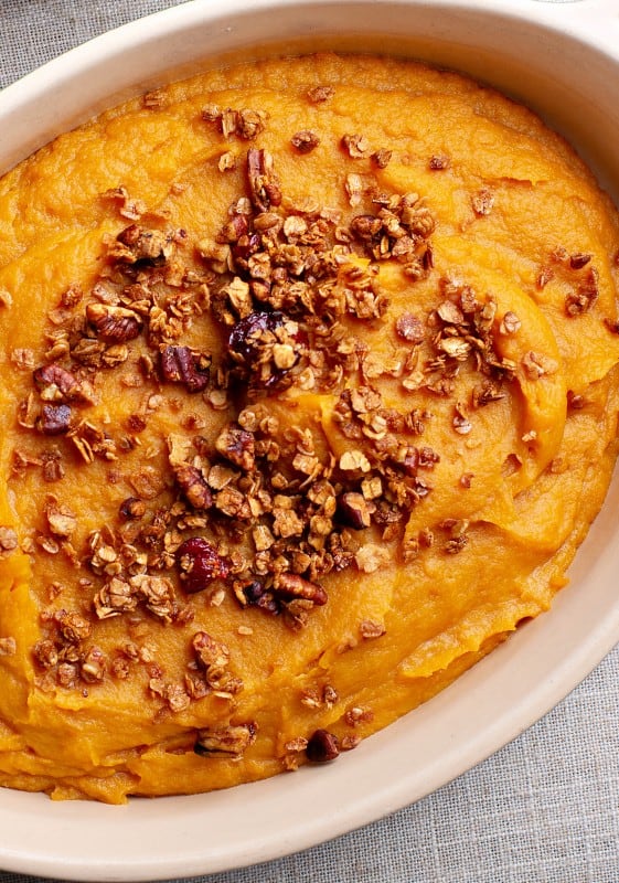 Close-up view of a sweet potato casserole, showing the golden-brown pecan topping and vibrant orange filling beneath.
