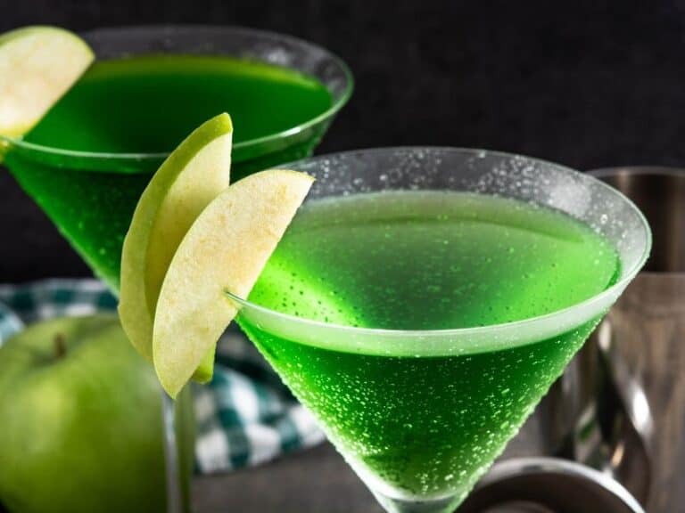 Appletini Cocktail in a Martini Glass. A visually appealing Appletini cocktail is served in a classic martini glass. The drink appears vibrant and refreshing, with a greenish hue. It is garnished with a slice of green apple, adding a touch of elegance to the presentation.