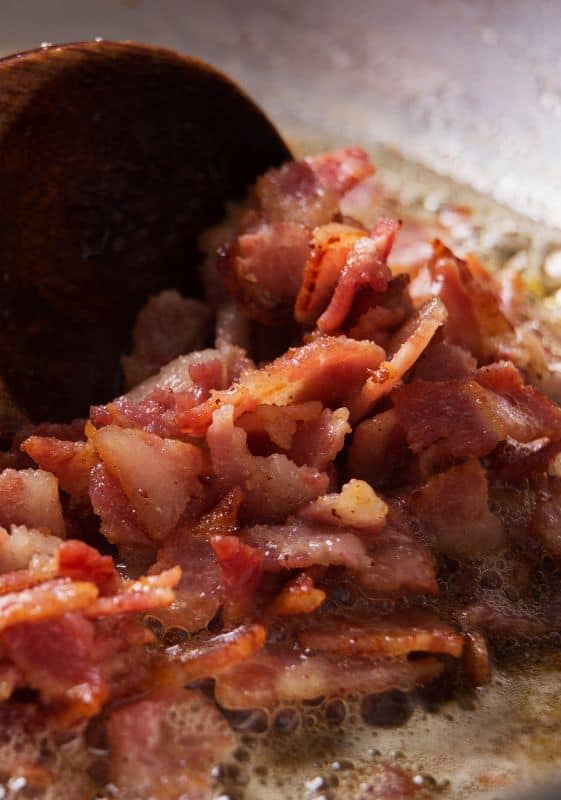 Searing Bacon in Skillet: Thick-cut bacon sizzling in a skillet, releasing its savory aroma.