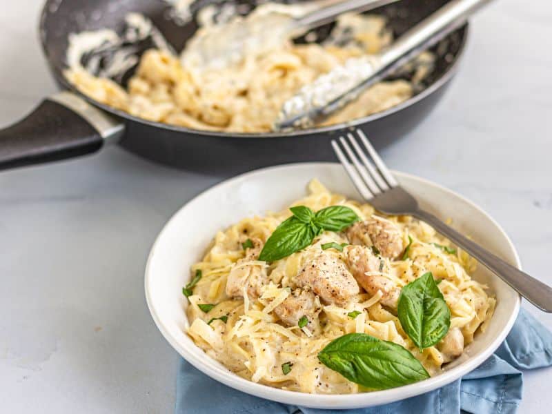 Skillet with al dente pasta, generously coated in creamy garlic sauce, ready to be enjoyed and a plate of Creamy Garlic Chicken Pasta garnished with fresh basil.