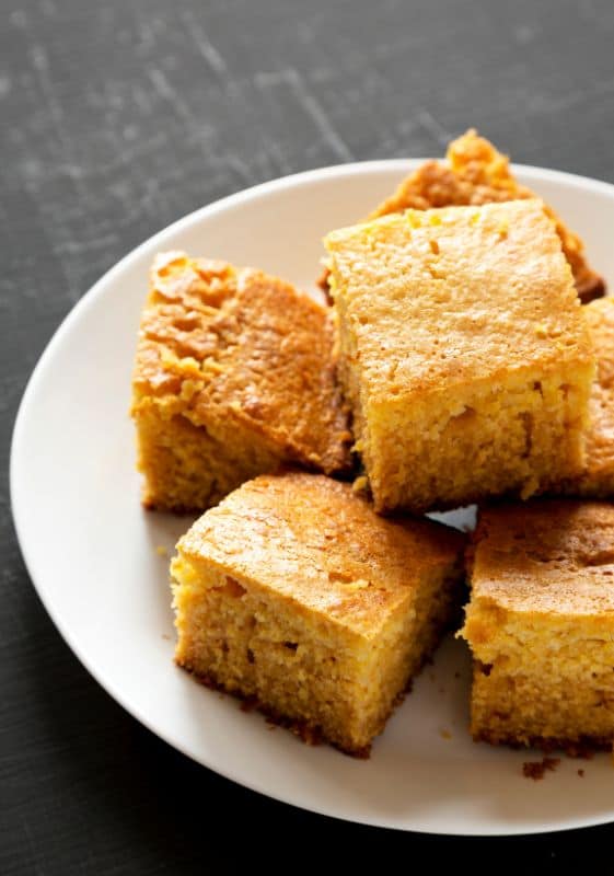 Homemade slices of cornbread on white plate ready to eat.