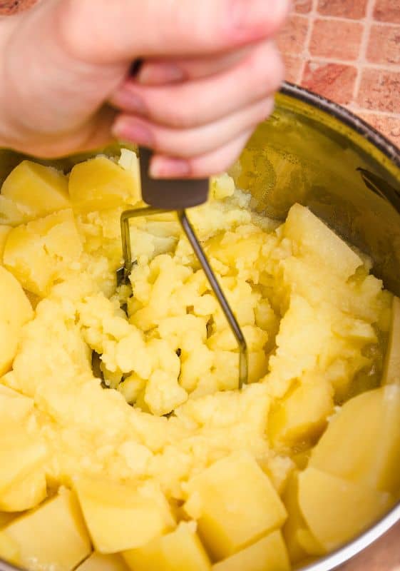 Mashing potatoes in a pan with a potato masher.