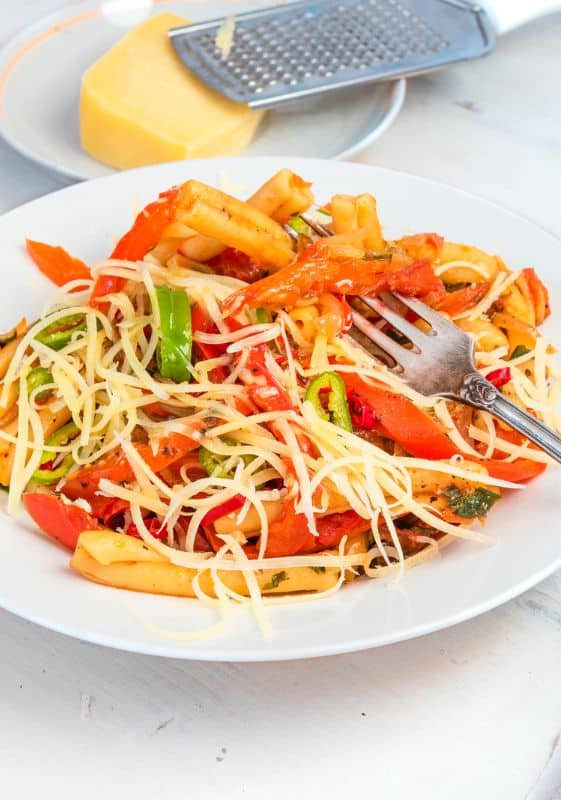 Rasta Pasta in a white plate and a fork. A beautifully presented Rasta Pasta dish on a white plate, artistically garnished with parmesan cheese. The creamy sauce gently clings to the pasta, adorned with colorful bell peppers, offering a delightful and appetizing sight.