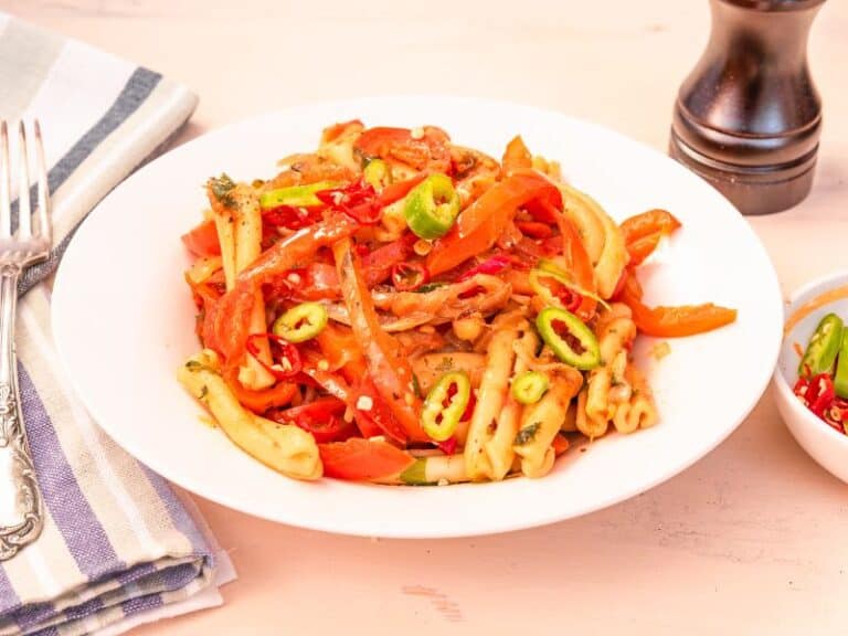 A captivating bowl of Rasta Pasta served with jerk chicken, showcasing the beautifully intertwined penne pasta coated in a creamy sauce. The dish is elevated by the colorful bell peppers, creating a feast for both the palate and the eyes.