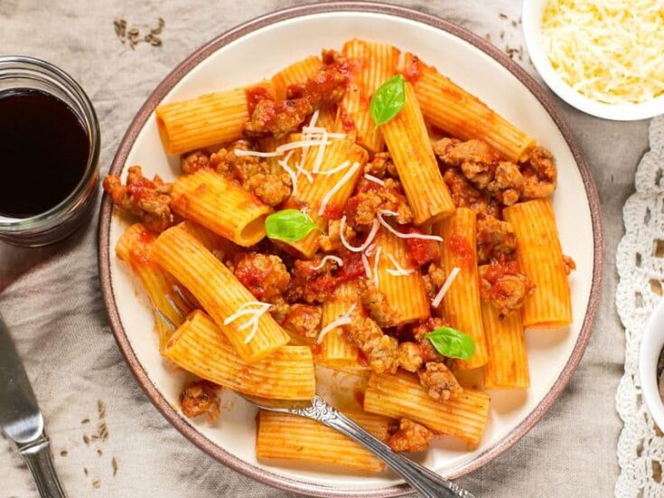 Deliciously rich and hearty Rigatoni Bolognese served in a white bowl, garnished with fresh basil leaves and Parmesan cheese.